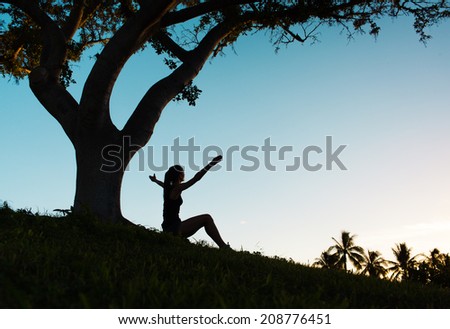 Silhouette of a woman with hands raised in the sunset.