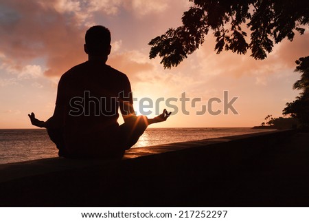 Man meditating in an yoga pose on the beach