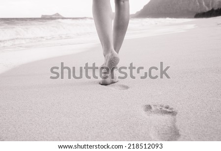 Beach travel - woman walking on sand beach leaving footprints in the sand. Closeup detail of female feet and beach in Hawaii