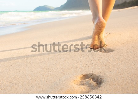 Woman walking on sand beach leaving footprints in the sand.