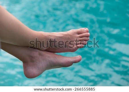Relaxed feet hanging over a clear blue water.