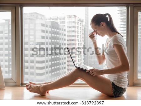 Tired young woman on her laptop in a city setting.