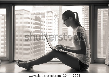 Woman using laptop next to a window with city view