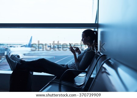 Woman waiting in airport terminal using her smartphone
