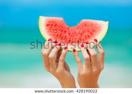 Hand holding watermelon on the beach.