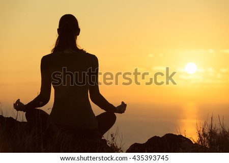 Female meditating overlooking the beautiful sunset. Healthy mind body and spirit concept.