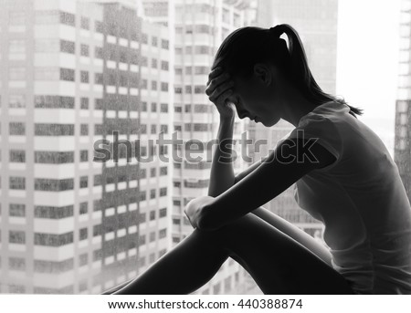 Sad and lonely woman in the city sitting next to a window.