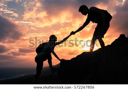 Giving a helping hand. Man helping female climber up a mountain.