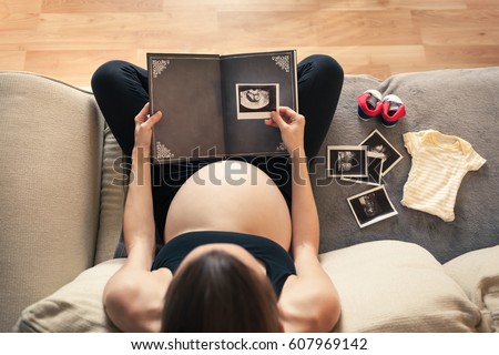 Pregnancy and becoming parent concept. Mother placing a ultrasound picture of her baby to a photo album.