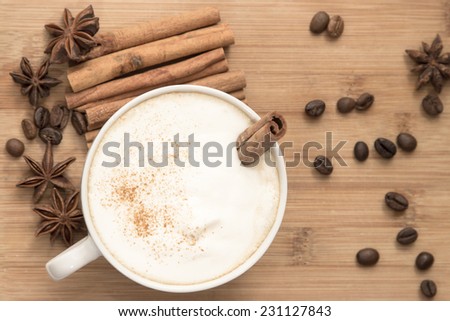 white cup of hot coffee with milk foam, cinnamon, star anise and coffee beans  on the wooden table