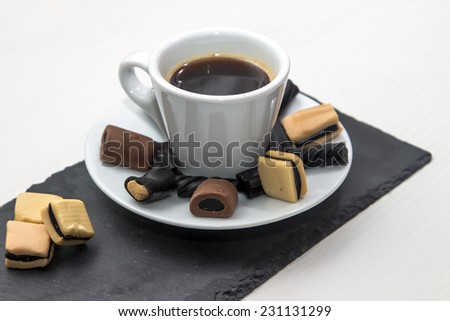 white cup of hot black coffee with gummy and licorice candy on the saucer, stand of slate