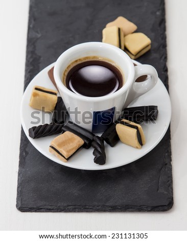 white cup of hot black coffee with gummy and licorice candy on the saucer, stand of slate