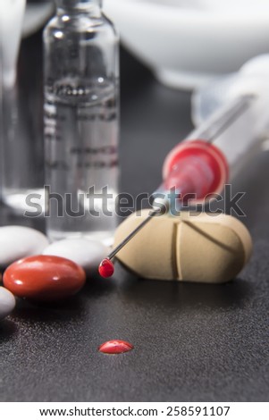 disposable syringe with medication and blood, glass capsules and color tablets on a black background