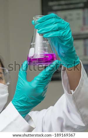 Hands in safety glove holding test glass with chemical inside