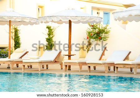 lounge chairs by the pool at sunset time.  Light Mediterranean-style bungalows