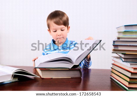 little boy opens a large book and looking into it boy 5 years. on the desk a lot of books. photo taken on a light background