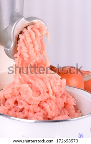 chicken meat is ground in a meat grinder in a bowl. near is onion. photo taken on a light background vertical