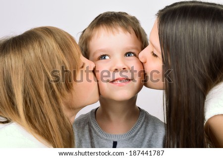 two girls kissing little smiling boy on the light background, horizontal