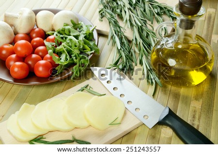 sliced cheese, tomatoes, mushrooms and herbs on a kitchen table top view closeup