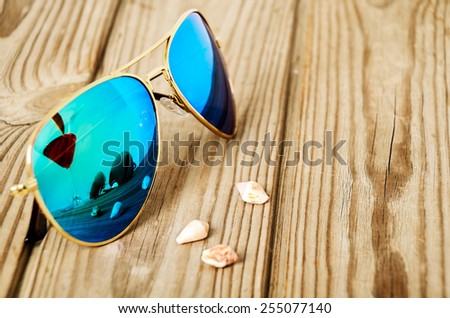 blue mirrored sunglasses wiht reflection of martini glass and shells on the wooden background close up. horizontal