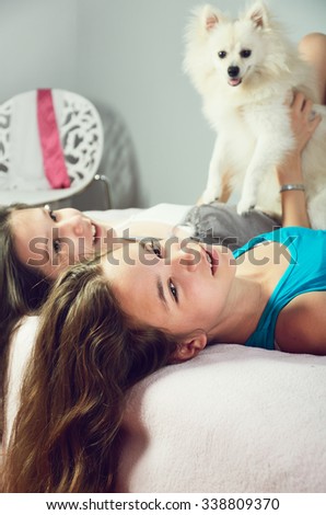 tinted image two girls with a Pomeranian lay on the bed and laughing close-up. vertical format