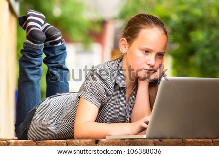 Young girl lying on the porch of the rural house with a laptop.