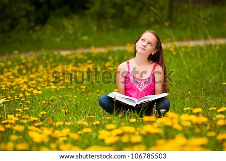 Girl sits on a grass and dreams while reading a book