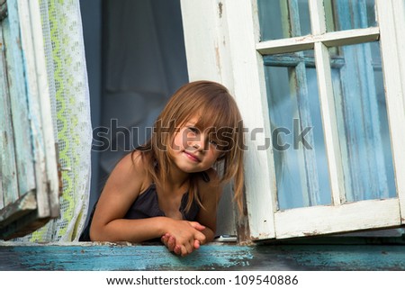 Little girl looks out the window rural house.