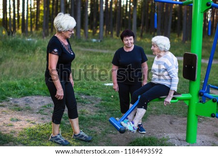 Elderly woman on a sports simulator, two women help her to do exercises.