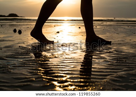 Feet of a young woman walking on the beach at sunset (backlit)