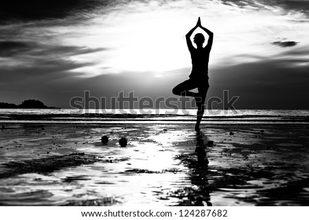 Black and white picture: Young woman practicing yoga on the beach at sunset.