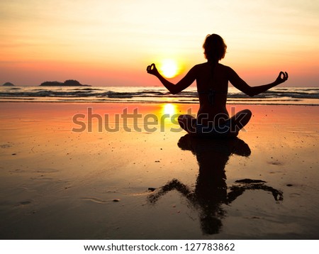 Young yoga woman sitting on sea coast at sunset