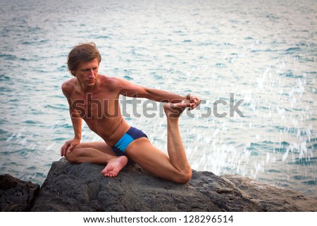 Young man doing yoga exercise on the deserted wild stone sea beach