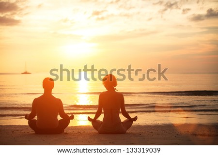 Young couple sitting on the beach of the sea in the lotus position at sunset, yoga practice