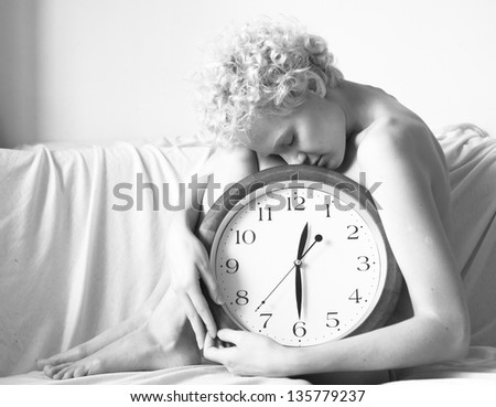 Conceptual portrait of woman in bed with big clock, black and white photo.