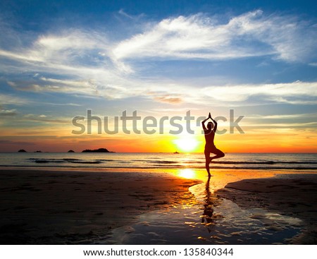 Silhouette of woman practicing yoga on the beach during a beautiful sunset
