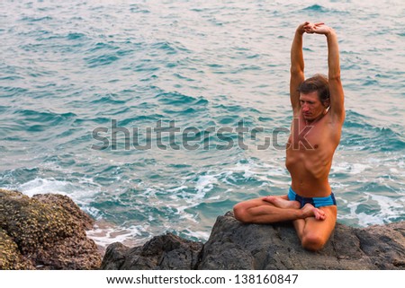 Young man doing yoga exercise on the deserted wild stone sea beach.