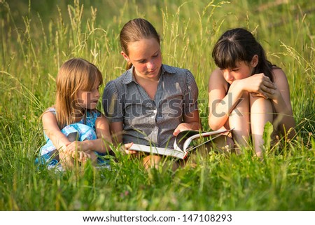 Children reading book in natural environment together.