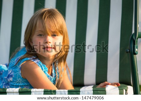 Close-up portrait of charming cheerful girl lying on a swing in the yard of a country house