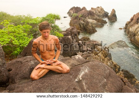 Man doing yoga exercise on the deserted wild stone sea beach.