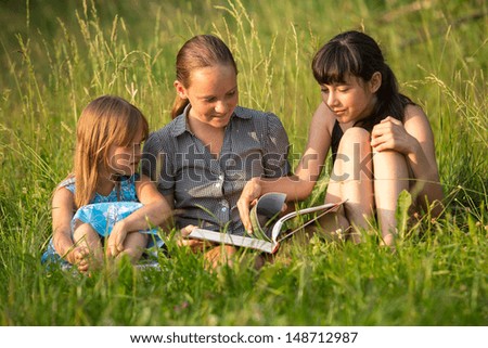 Three little sister reading book in natural environment together.