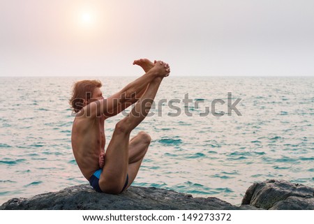 Young man doing yoga exercise (on the deserted wild stone sea beach)