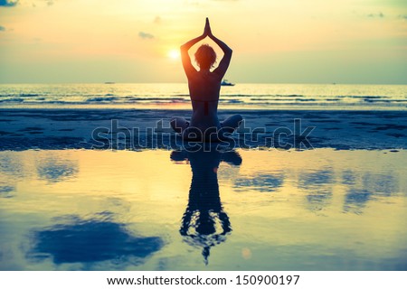Yoga woman sitting in lotus pose on the beach during sunset, with reflection in water (cross-process style)