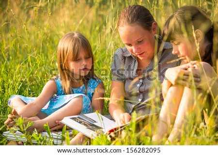 Portrait of three cute little girls reading book in natural environment together.
