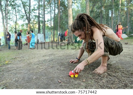 PSKOV REGION, RUSSIA - JULY 19: A member of the Russian Rainbow Family (Youth counterculture 1960\'s: bohemianism, hipster and hippie culture) playing with a toy car during an annual gathering near Lake Asho on July 19, 2010 in Pskov Region, Russia.