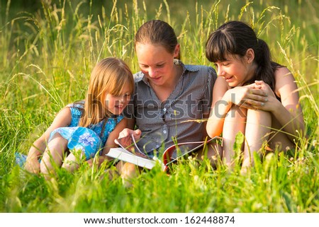 Three cute little girls reading book in natural environment together.