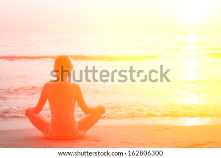 Yoga woman sitting in lotus pose on the beach during sunset, in bright colors.