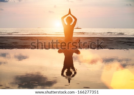 Yoga woman sitting in lotus pose on the beach during sunset, with reflection in water, bright colors.