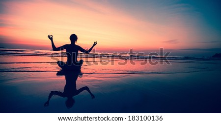 Silhouette of a woman yoga sitting on sea coast at surreal sunset.