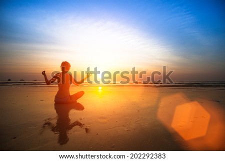 Silhouette yoga woman sitting on sea coast at beautiful sunset.
